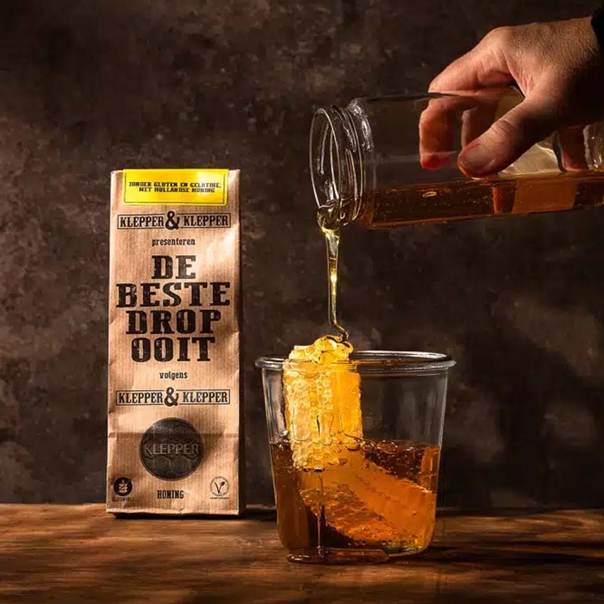 Foto van een zakje honingdrop van Klepper en Klepper met een glas vol honing en een echte honingraat.