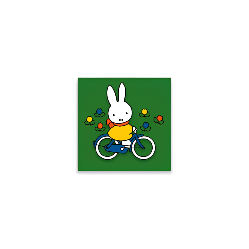 Miffy® kylskåpsmagnet i två lager MDF med mörkgrön bakgrund, små tulpaner och utfräst motiv av Miffy på cykel.