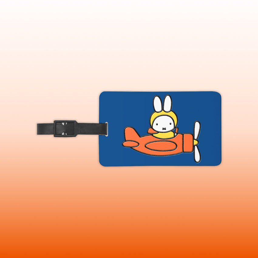 Miffy® bagagebricka i mörkblå silikon med reliefmotiv av Miffy i orange propellerflygplan och gul pilotmössa.
