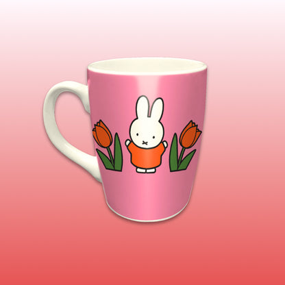 Miffy® Relax mugg i offwhite keramik med mörkrosa bakgrund, orange tulpaner och Miffy-motiv på båda sidor av muggen.