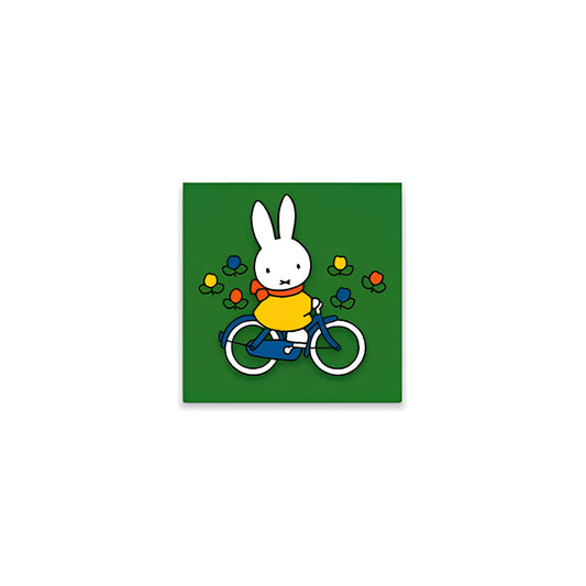Miffy® kylskåpsmagnet i två lager MDF med mörkgrön bakgrund, små tulpaner och utfräst motiv av Miffy på cykel.