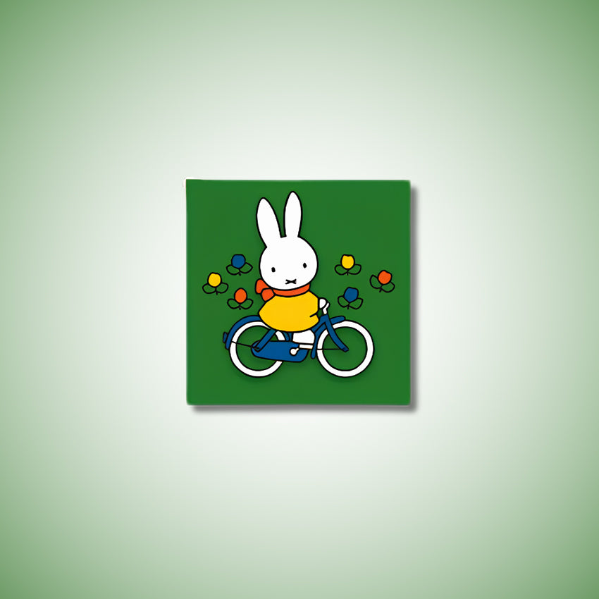 Miffy® kylskåpsmagnet i två lager MDF med mörkgrön bakgrund, små tulpaner och utfräst motiv av Miffy på cykel.