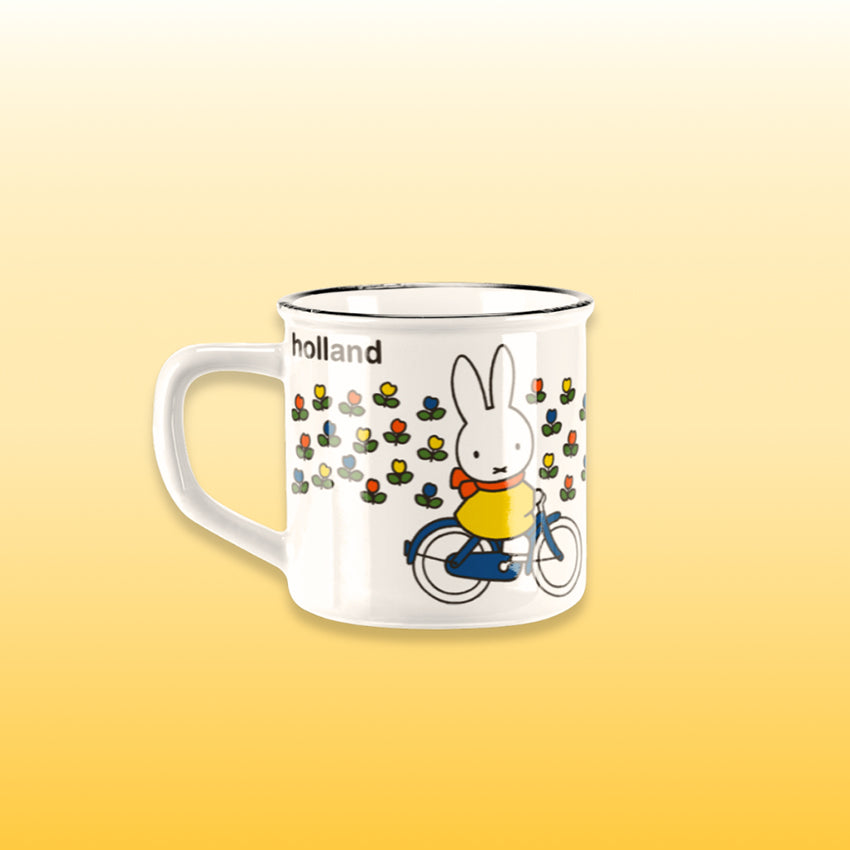 Miffy® retro mugg i offwhite keramik med svart kant och motiv av Miffy på cykel genom ett holländskt tulpanfält med orange-röd halsduk.